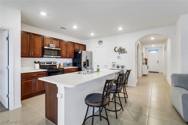 kitchen featuring a kitchen bar, appliances with stainless steel finishes, sink, light tile patterned floors, and an island with sink