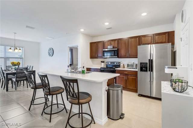 kitchen featuring appliances with stainless steel finishes, a kitchen island with sink, sink, an inviting chandelier, and hanging light fixtures