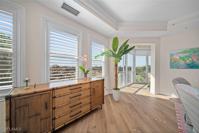 living area with light hardwood / wood-style floors, crown molding, a tray ceiling, and a healthy amount of sunlight