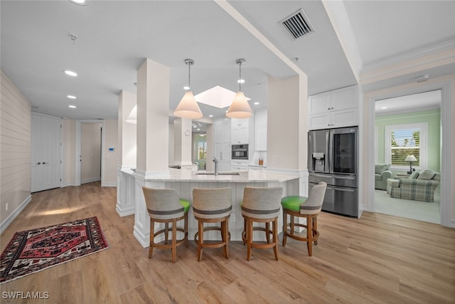 kitchen featuring appliances with stainless steel finishes, light stone counters, light hardwood / wood-style flooring, white cabinets, and hanging light fixtures