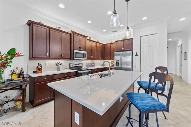 kitchen with pendant lighting, stainless steel appliances, ornamental molding, and an island with sink