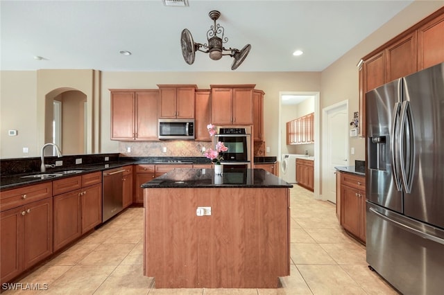 kitchen with sink, a kitchen island, dark stone counters, and appliances with stainless steel finishes