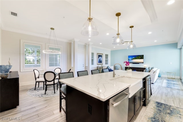 kitchen featuring light stone countertops, dishwasher, light hardwood / wood-style floors, decorative light fixtures, and a kitchen island with sink