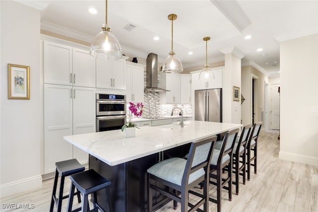 kitchen with light stone countertops, wall chimney exhaust hood, stainless steel appliances, a large island with sink, and white cabinets