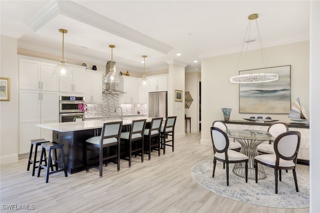 kitchen featuring appliances with stainless steel finishes, wall chimney range hood, decorative light fixtures, light hardwood / wood-style flooring, and white cabinetry