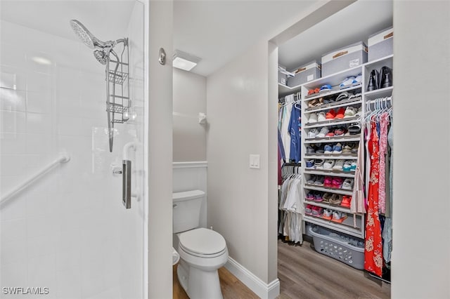 full bath with a spacious closet, toilet, a stall shower, wood finished floors, and baseboards