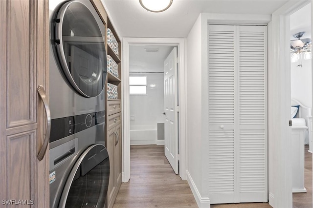 laundry room featuring stacked washer and clothes dryer, light wood-style flooring, baseboards, and laundry area