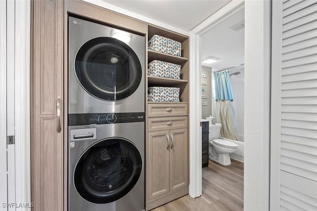 clothes washing area featuring stacked washer and dryer, cabinet space, and light wood finished floors