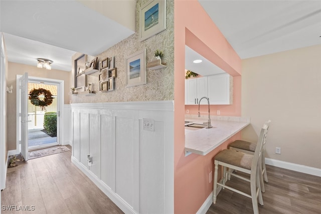 bar with wallpapered walls, baseboards, wainscoting, wood finished floors, and a sink