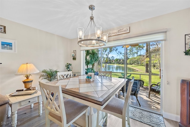 dining area with baseboards, a water view, an inviting chandelier, and wood finished floors