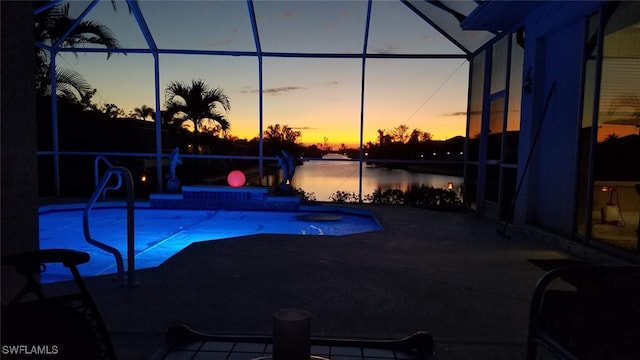 pool at dusk featuring glass enclosure, a water view, and a patio