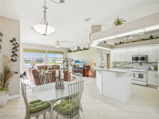 kitchen with white cabinetry, ceiling fan, hanging light fixtures, white range oven, and an island with sink