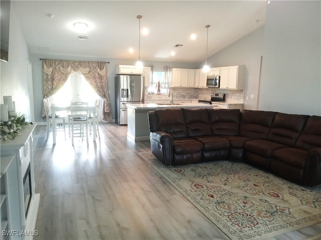 living room featuring light wood-type flooring, sink, and vaulted ceiling