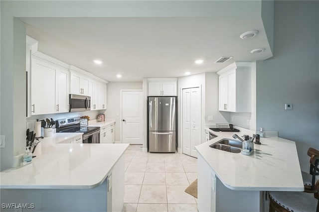 kitchen with light tile patterned floors, a kitchen breakfast bar, kitchen peninsula, white cabinets, and appliances with stainless steel finishes