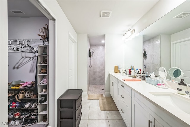 bathroom featuring tile patterned flooring, a tile shower, and vanity