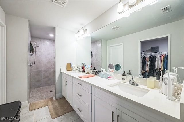 bathroom featuring tile patterned flooring, a tile shower, and vanity