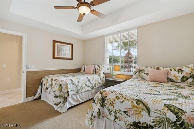 bedroom featuring a tray ceiling, light tile patterned floors, baseboards, and ceiling fan