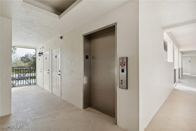 hallway with elevator and a textured ceiling