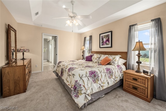 bedroom featuring a tray ceiling, ensuite bath, ceiling fan, and light colored carpet