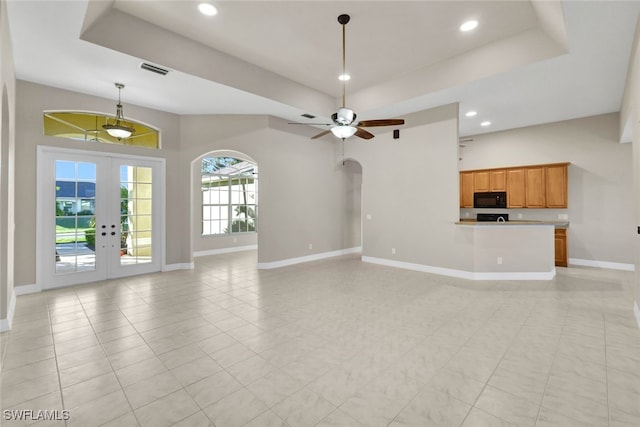 unfurnished living room featuring a tray ceiling, ceiling fan, and french doors