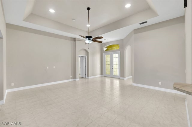 empty room featuring a tray ceiling, ceiling fan, and french doors