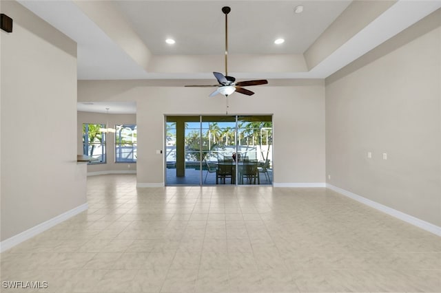 tiled spare room with ceiling fan with notable chandelier, a healthy amount of sunlight, and a tray ceiling