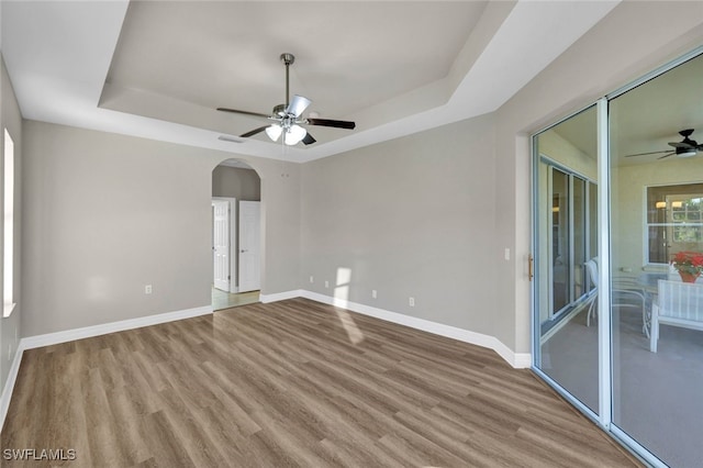 spare room featuring a tray ceiling, ceiling fan, and light wood-type flooring