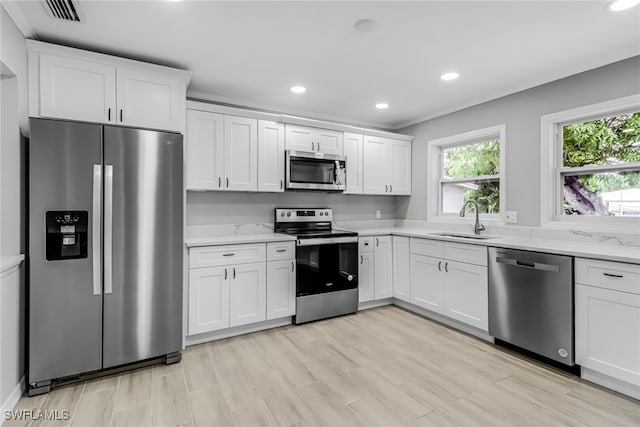 kitchen featuring light stone countertops, light wood-type flooring, stainless steel appliances, sink, and white cabinets