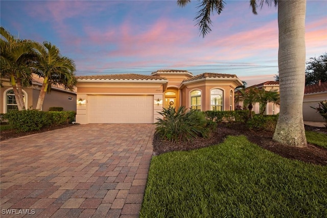 mediterranean / spanish-style house featuring a garage, decorative driveway, a tile roof, and stucco siding