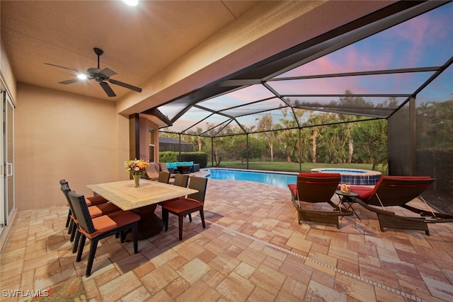 pool at dusk with glass enclosure, ceiling fan, a patio, and an in ground hot tub