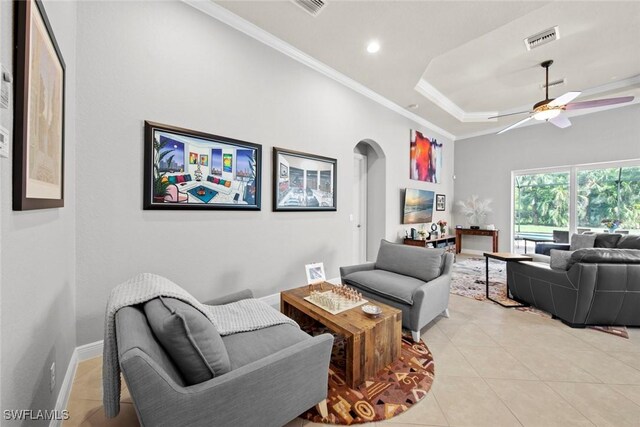 living room featuring a raised ceiling, ceiling fan, light tile patterned flooring, and ornamental molding