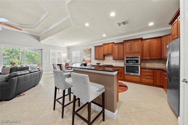 kitchen featuring a breakfast bar, stainless steel appliances, a raised ceiling, and an island with sink