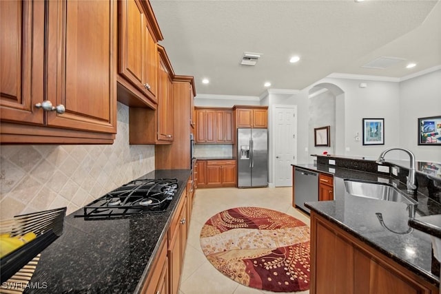 kitchen featuring appliances with stainless steel finishes, tasteful backsplash, sink, dark stone countertops, and ornamental molding