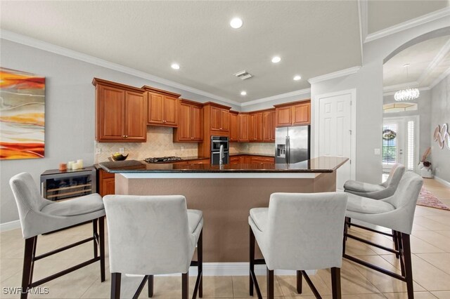 kitchen featuring decorative backsplash, ornamental molding, stainless steel appliances, a kitchen island with sink, and light tile patterned flooring