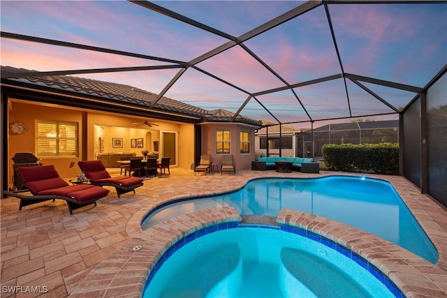 pool at dusk with an outdoor living space, glass enclosure, and a patio area