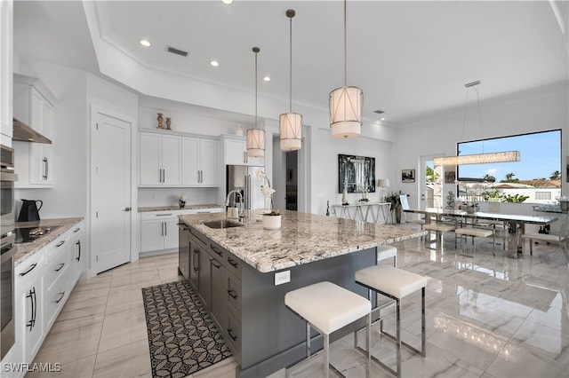 kitchen with pendant lighting, a large island with sink, white cabinets, a kitchen breakfast bar, and sink