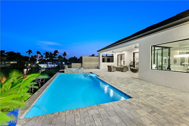 pool at dusk with a patio area, a water view, and an outdoor hangout area