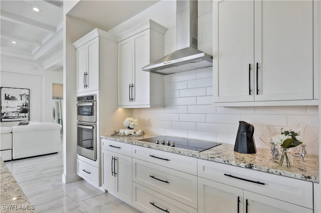 kitchen featuring black electric stovetop, wall chimney exhaust hood, double oven, tasteful backsplash, and white cabinetry