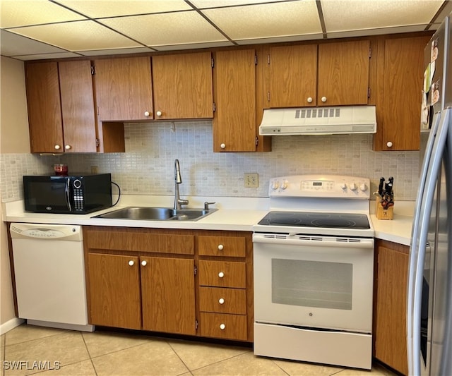 kitchen featuring a paneled ceiling, tasteful backsplash, white appliances, sink, and light tile patterned flooring