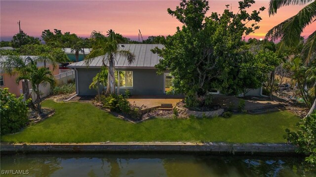 back house at dusk featuring a water view and a lawn