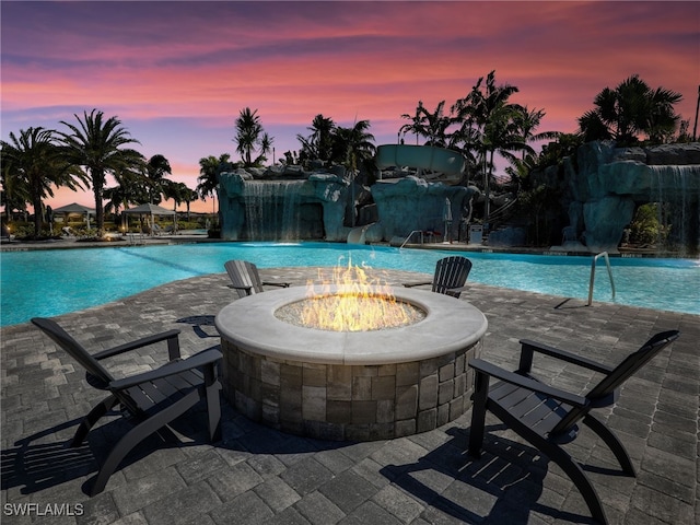 pool at dusk featuring pool water feature, an outdoor fire pit, and a patio area