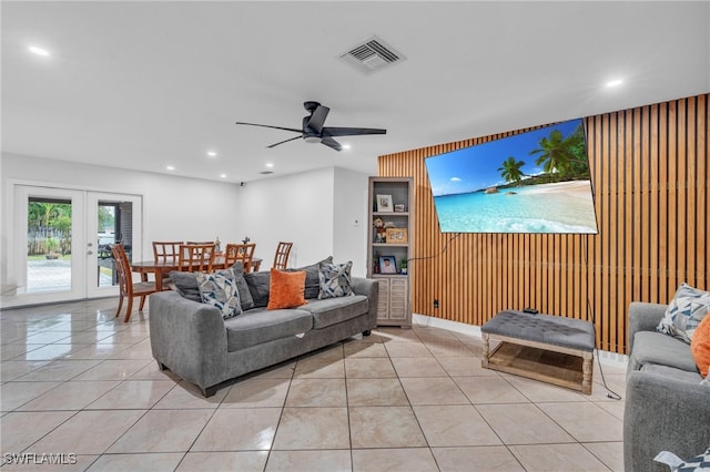 tiled living room featuring ceiling fan, wood walls, and french doors