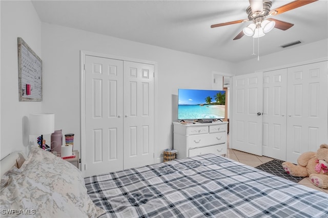 bedroom featuring ceiling fan, light tile patterned floors, and two closets