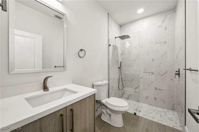 bathroom with tiled shower, toilet, vanity, and hardwood / wood-style flooring