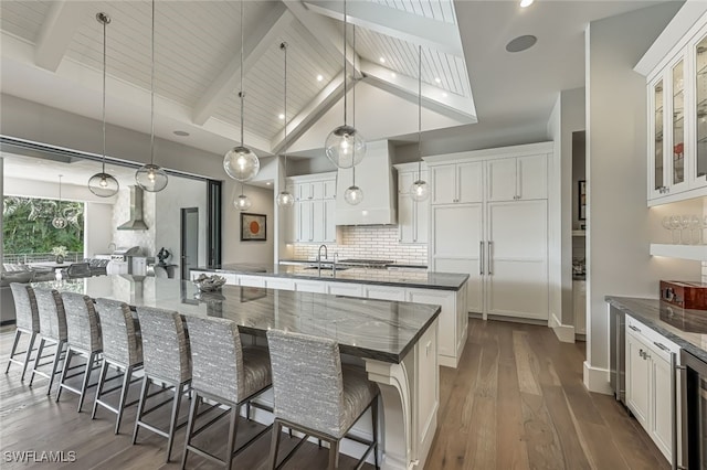 kitchen with a large island, pendant lighting, beam ceiling, white cabinetry, and a breakfast bar area