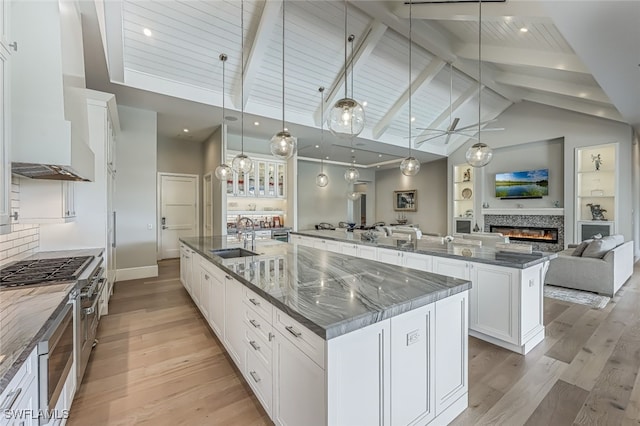 kitchen with custom range hood, a large island with sink, pendant lighting, light hardwood / wood-style floors, and white cabinetry