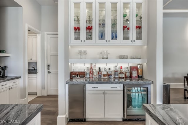 bar featuring dark stone counters, beverage cooler, white cabinets, dark hardwood / wood-style floors, and stainless steel refrigerator