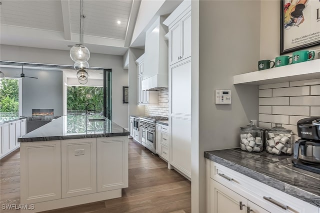 kitchen featuring pendant lighting, double oven range, decorative backsplash, an island with sink, and plenty of natural light