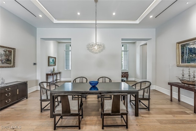 dining space with a raised ceiling, light wood-type flooring, and an inviting chandelier