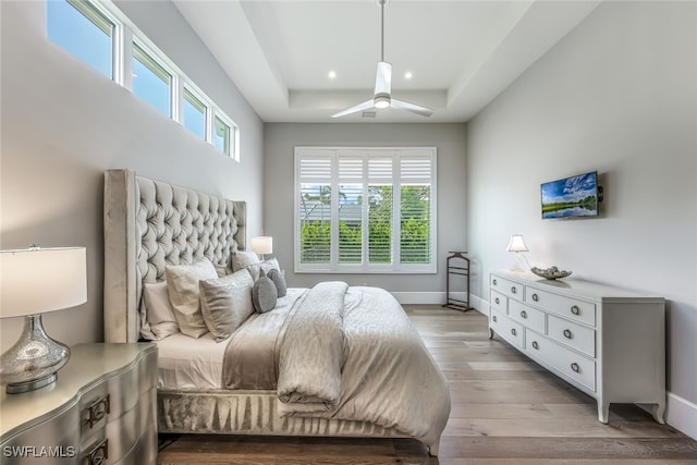 bedroom with ceiling fan, light hardwood / wood-style floors, and a raised ceiling